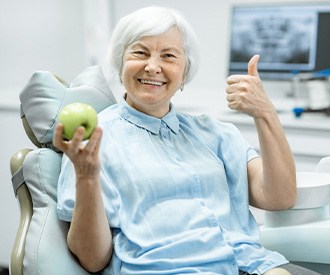A smiling older woman holding a green apple in a dentist’s office