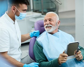 Senior patient looking at dentist while holding small mirror