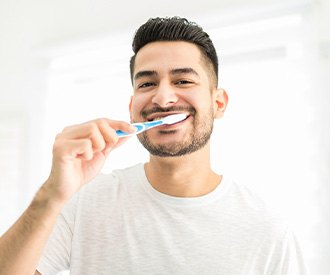 Man smiling while brushing his teeth