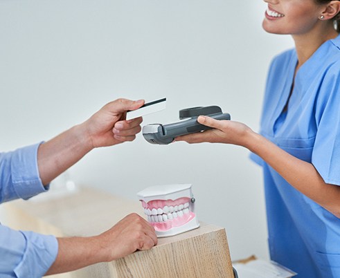 Man holding out card to payment device held by woman at desk with model teeth