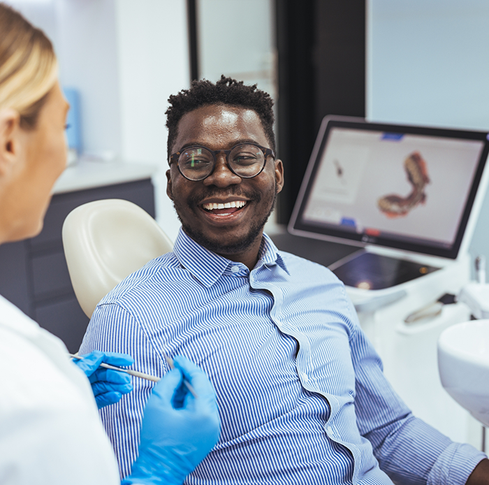 Man in button up shirt sitting in dental chair and smiling