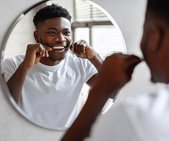 Man smiling while flossing his teeth in bathroom